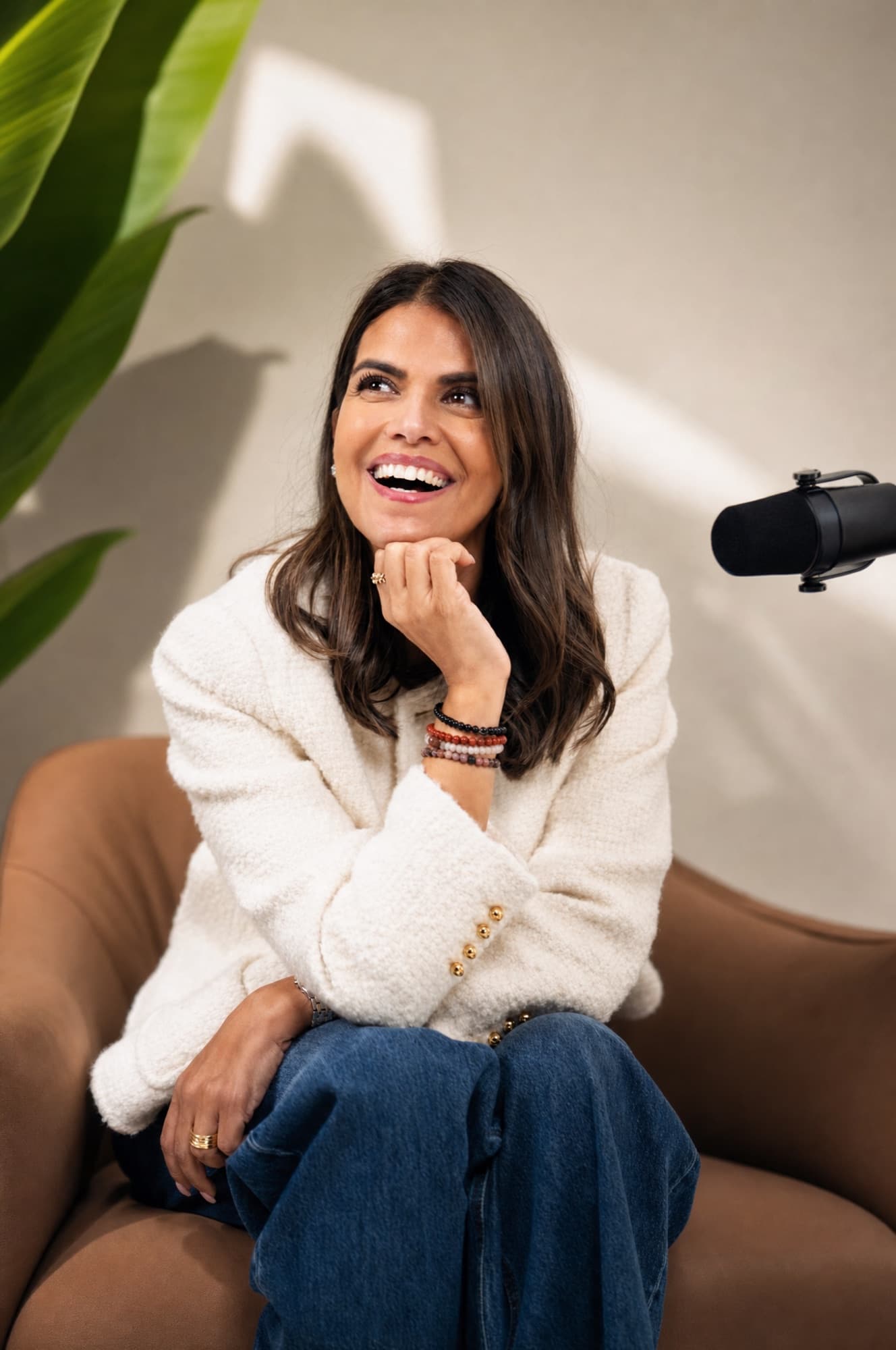Zahra Abdalla laughing in an armchair beside a podcast microphone.